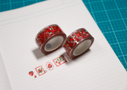 Two rolls of washi tape with a red and green strawberry pattern, displayed on a lined sheet of paper over a green cutting mat.