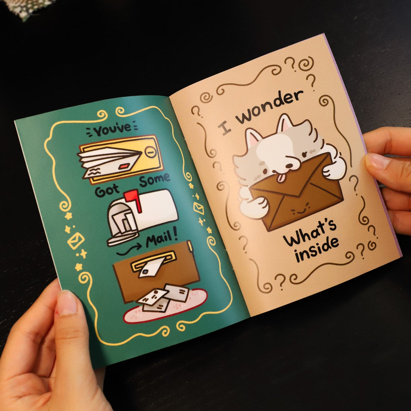 Two cartoon-style greeting cards held open by a hand on a dark surface.