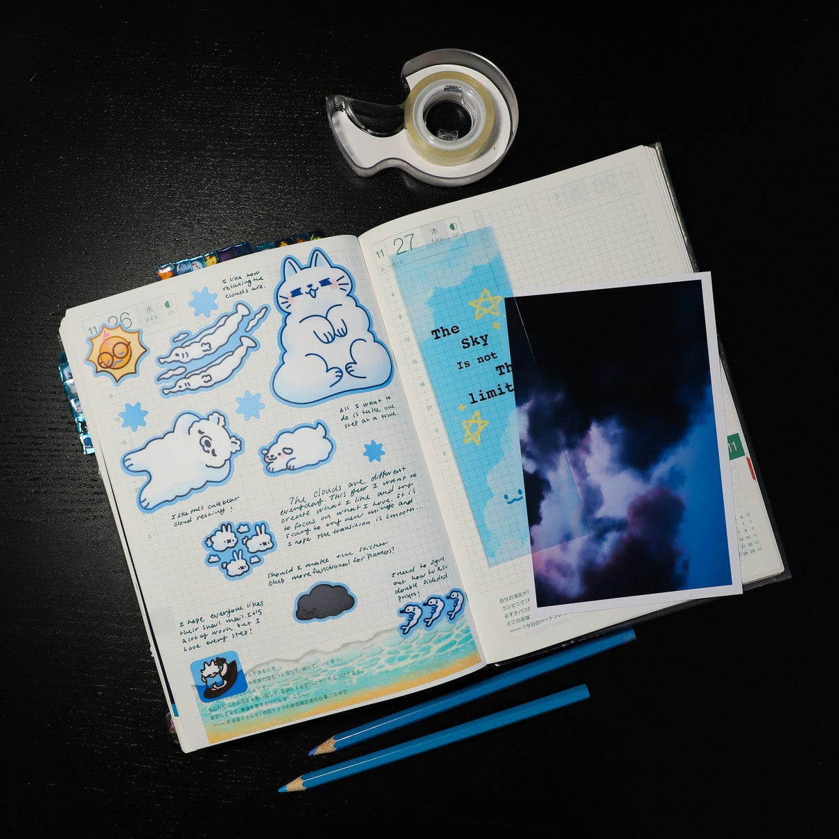 Open notebook with stickers, a photo, and stationery on a dark surface