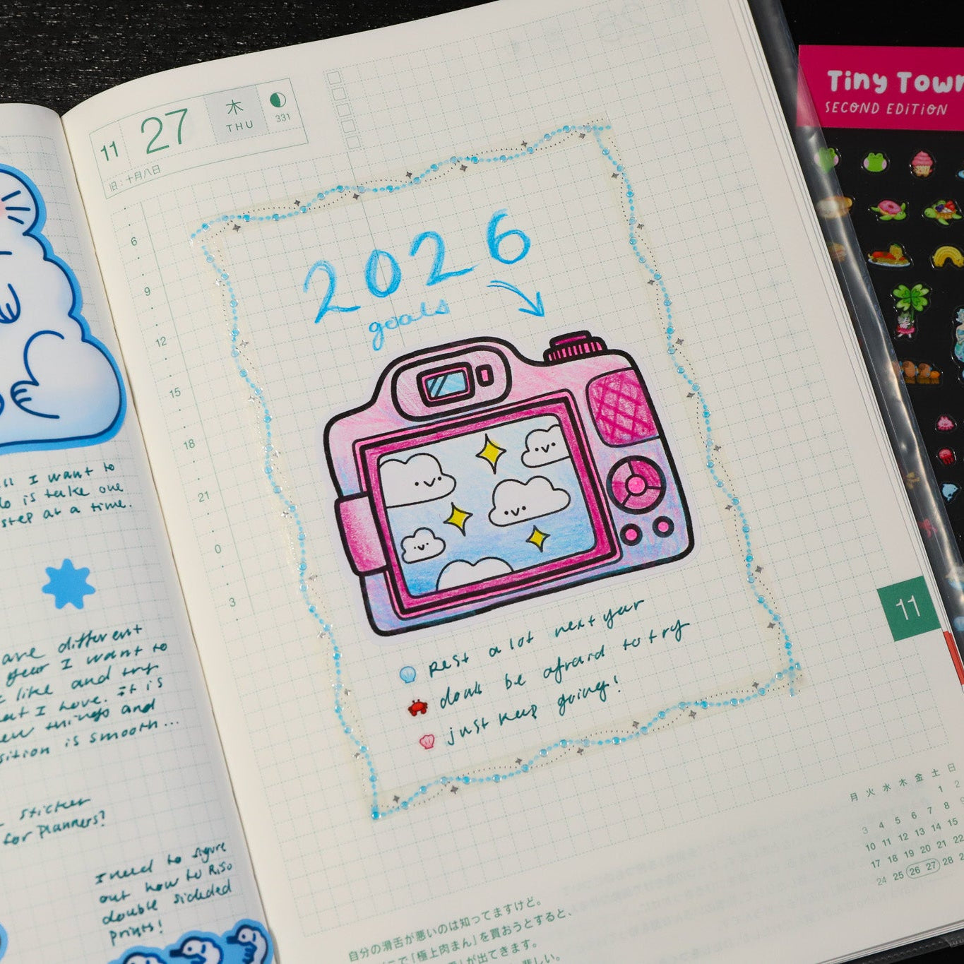 Open notebook with a drawing of a camera and '2026' text, surrounded by stickers.