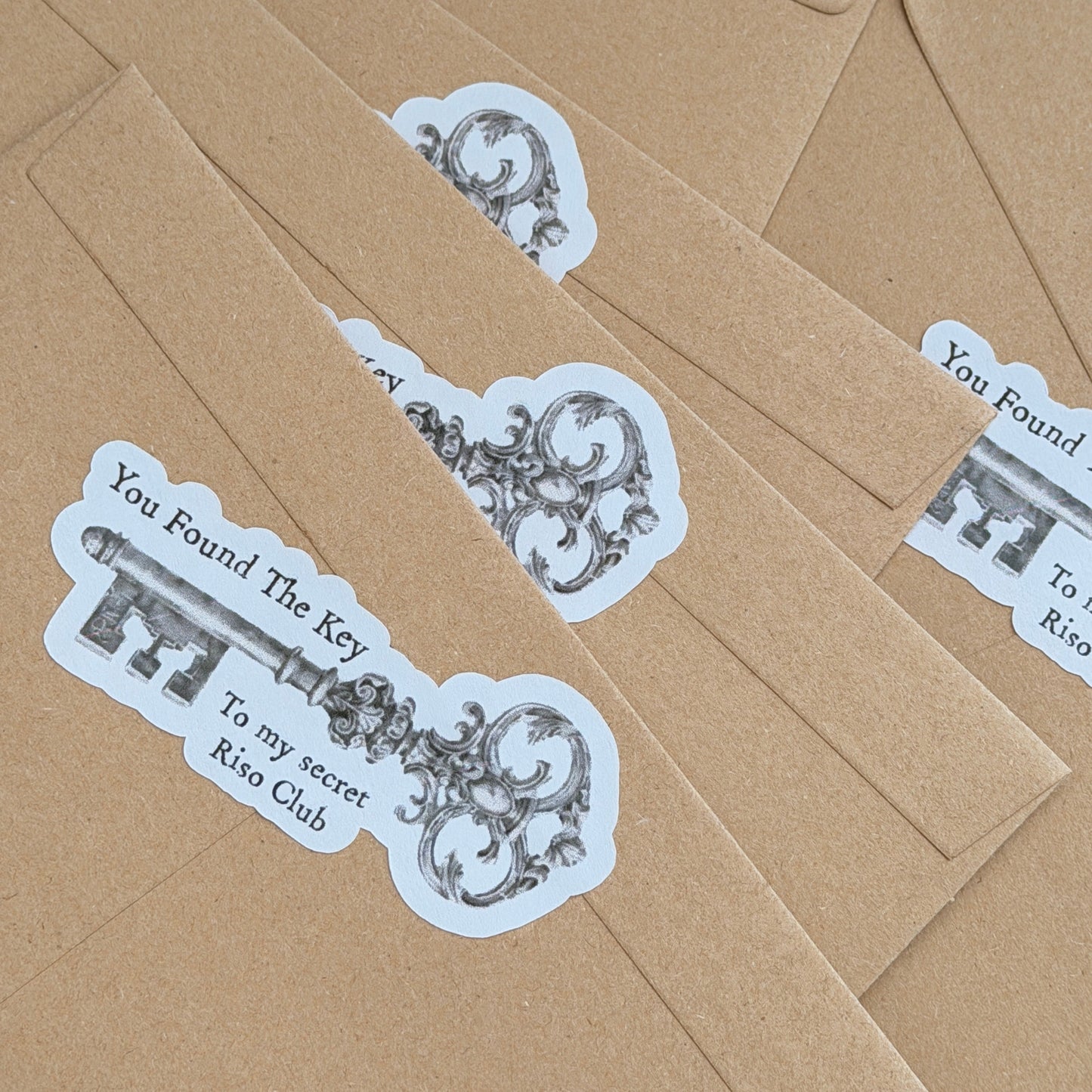 RISO print club monthly snail mail subscription. Kraft paper envelopes with decorative key stickers on a matching brown background
