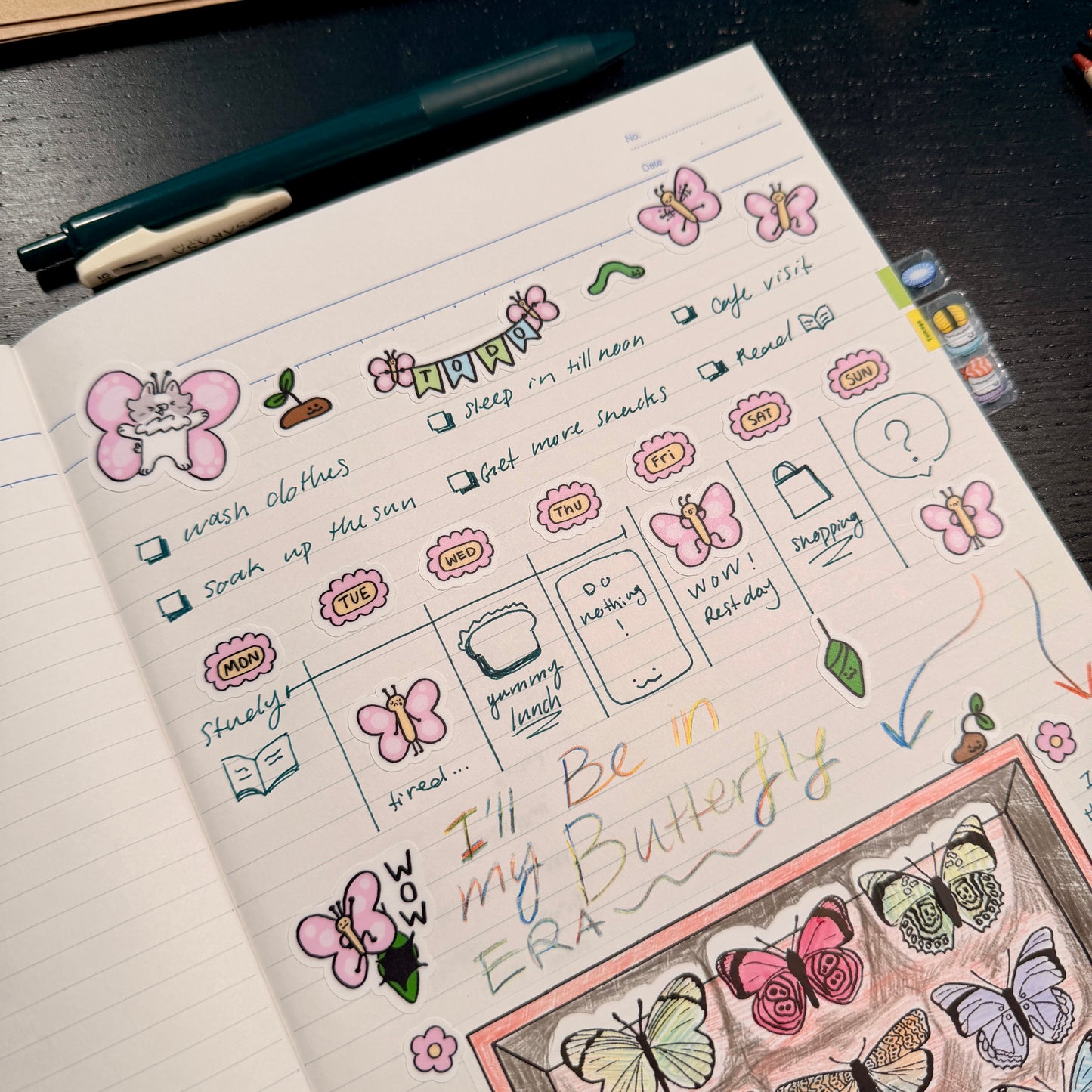 Notebook page with butterfly-themed stickers and doodles on a dark surface.