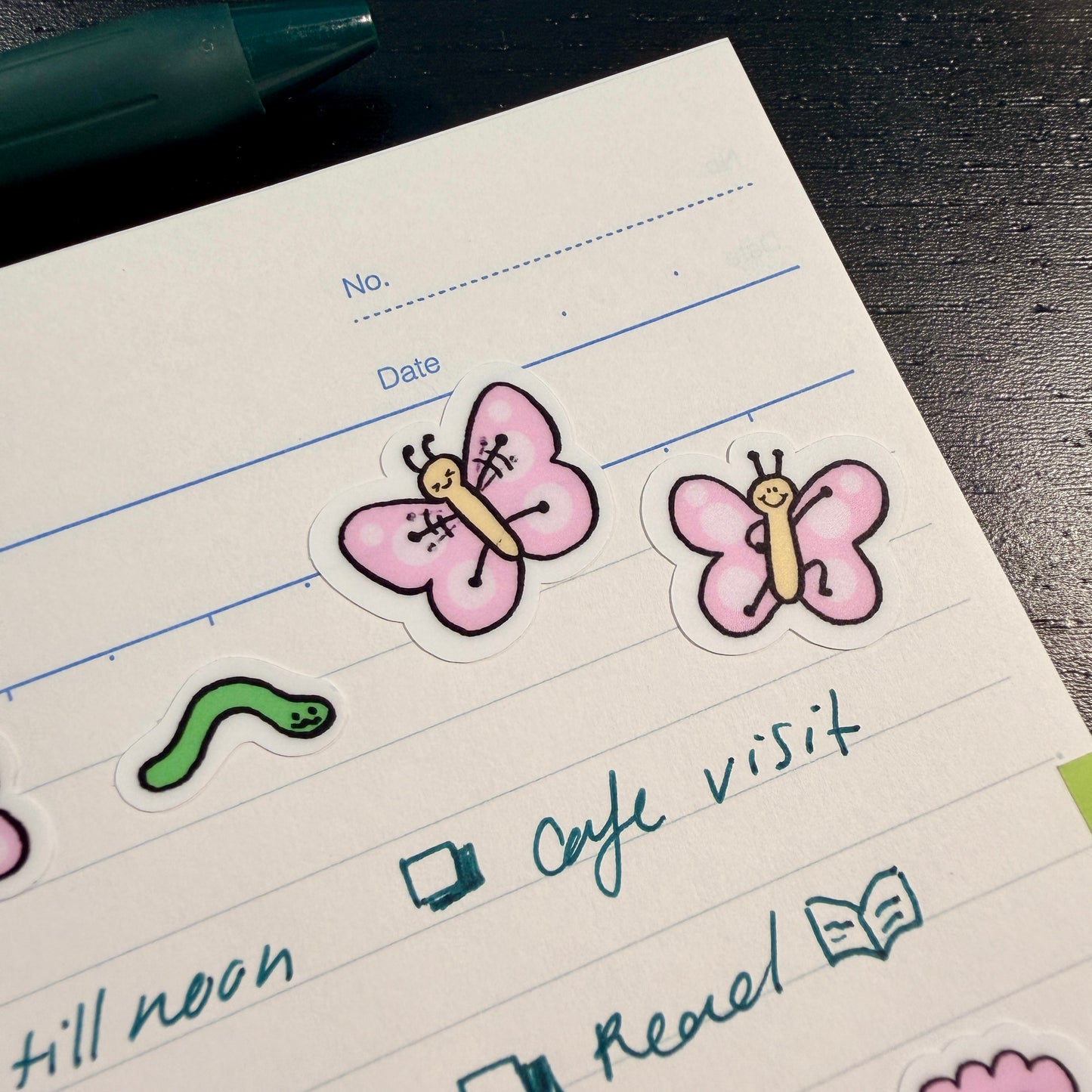 Notebook with stickers of butterflies and a worm on lined paper.