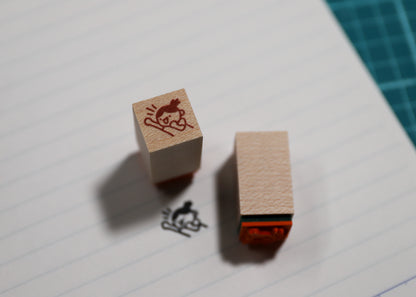 A wooden rubber stamp and its inked impression on lined paper, with a green cutting mat visible in the background corner.