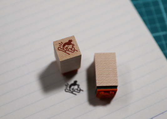 A wooden rubber stamp and its inked impression on lined paper, with a green cutting mat visible in the background corner.